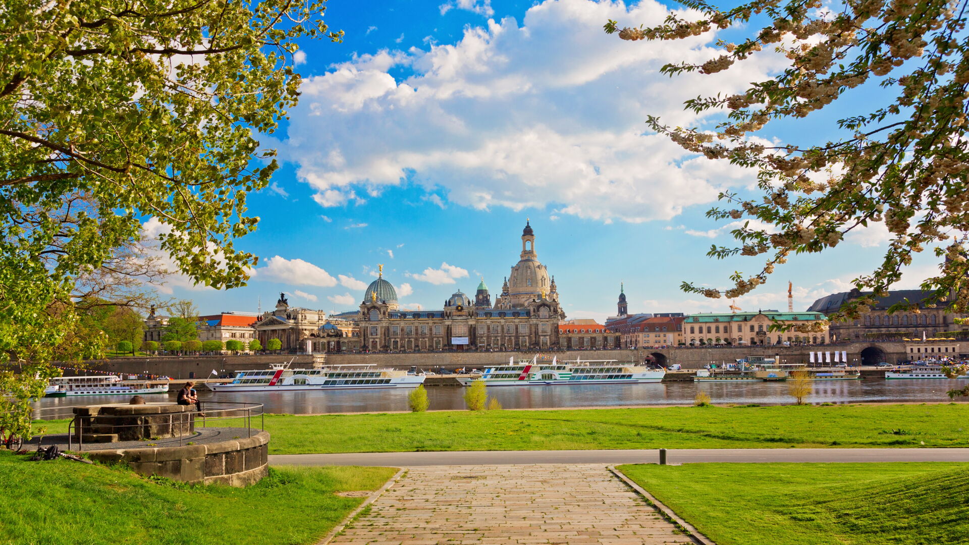 Panoramablick auf die historische Skyline von Dresden mit Frauenkirche, Zwinger und der Elbe unter blauem Himmel mit Wolken.