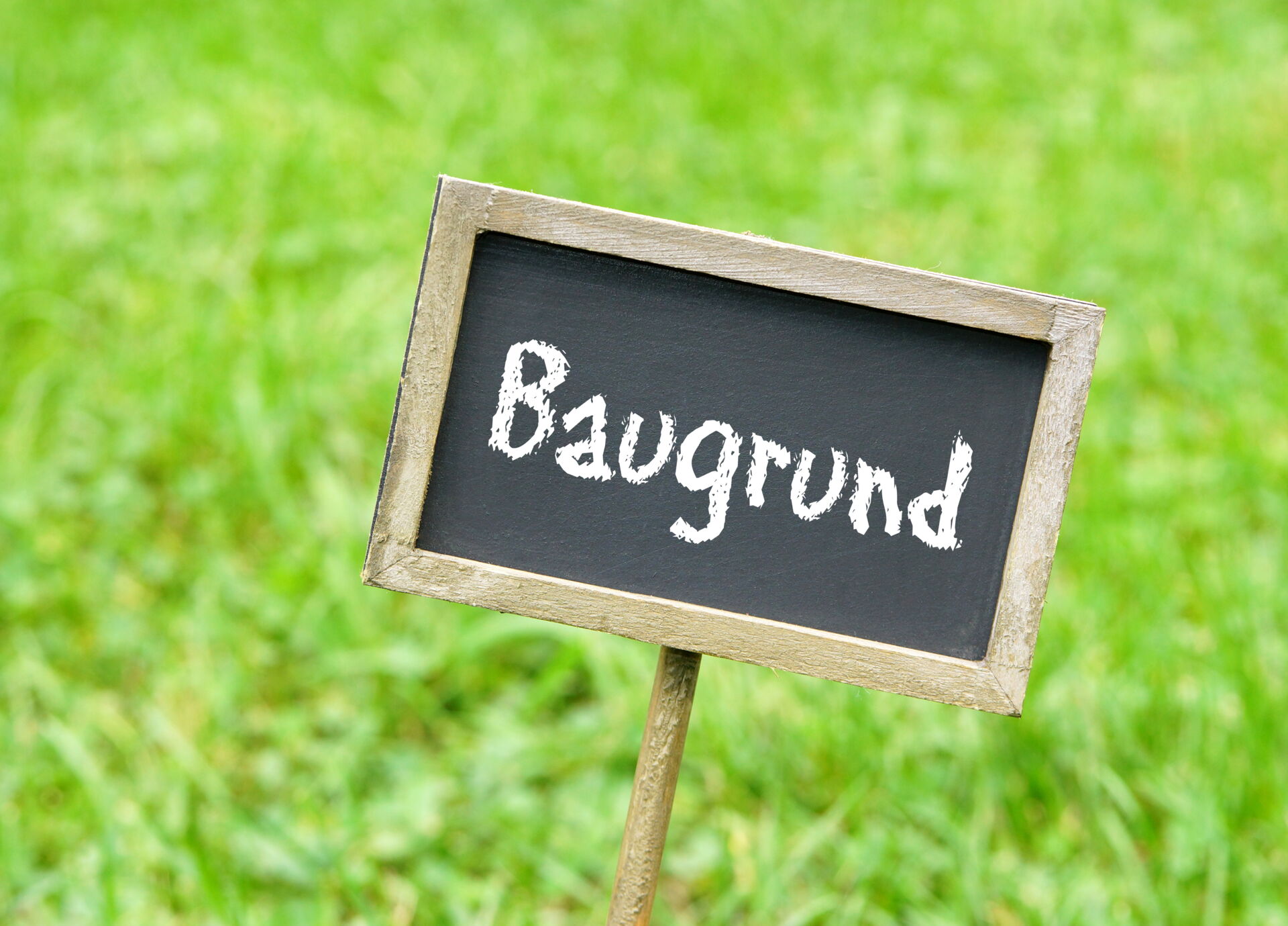 Ein kleines schwarzes Schild mit der weißen Aufschrift "Baugrund" steckt in einer grünen Wiese.