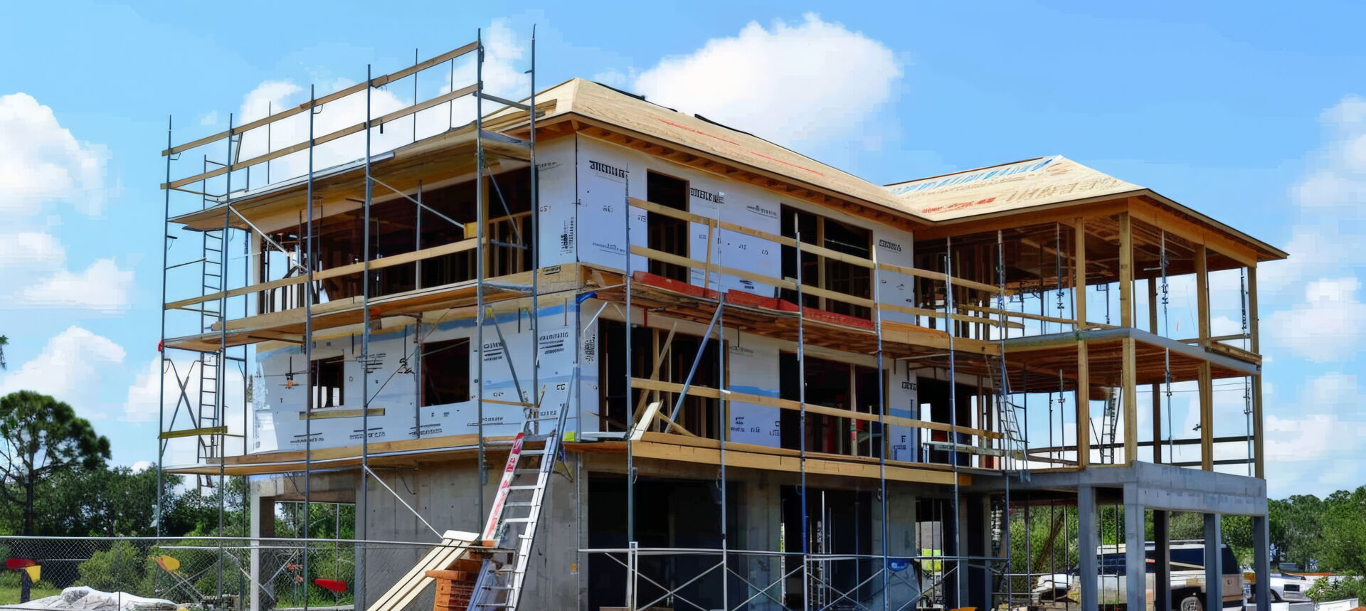 Ein zweistöckiges Haus im Rohbau mit Gerüst und unfertigem Dach unter blauem Himmel auf einer Baustelle in Polen.